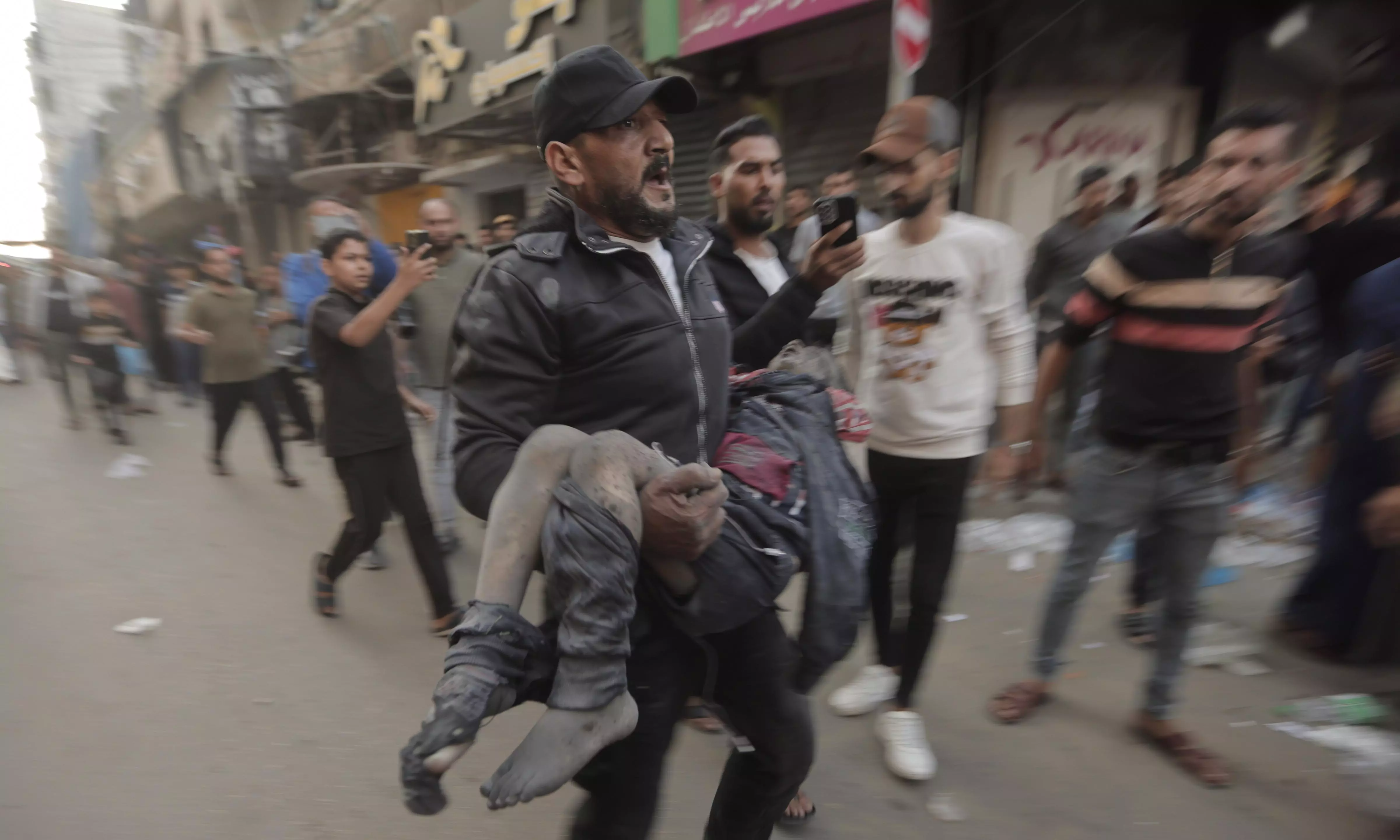 A Palestinian man runs with an injured boy following an Israeli airstrike in Khan Younis refugee camp, southern Gaza Strip, on November 18 | AP/PTI