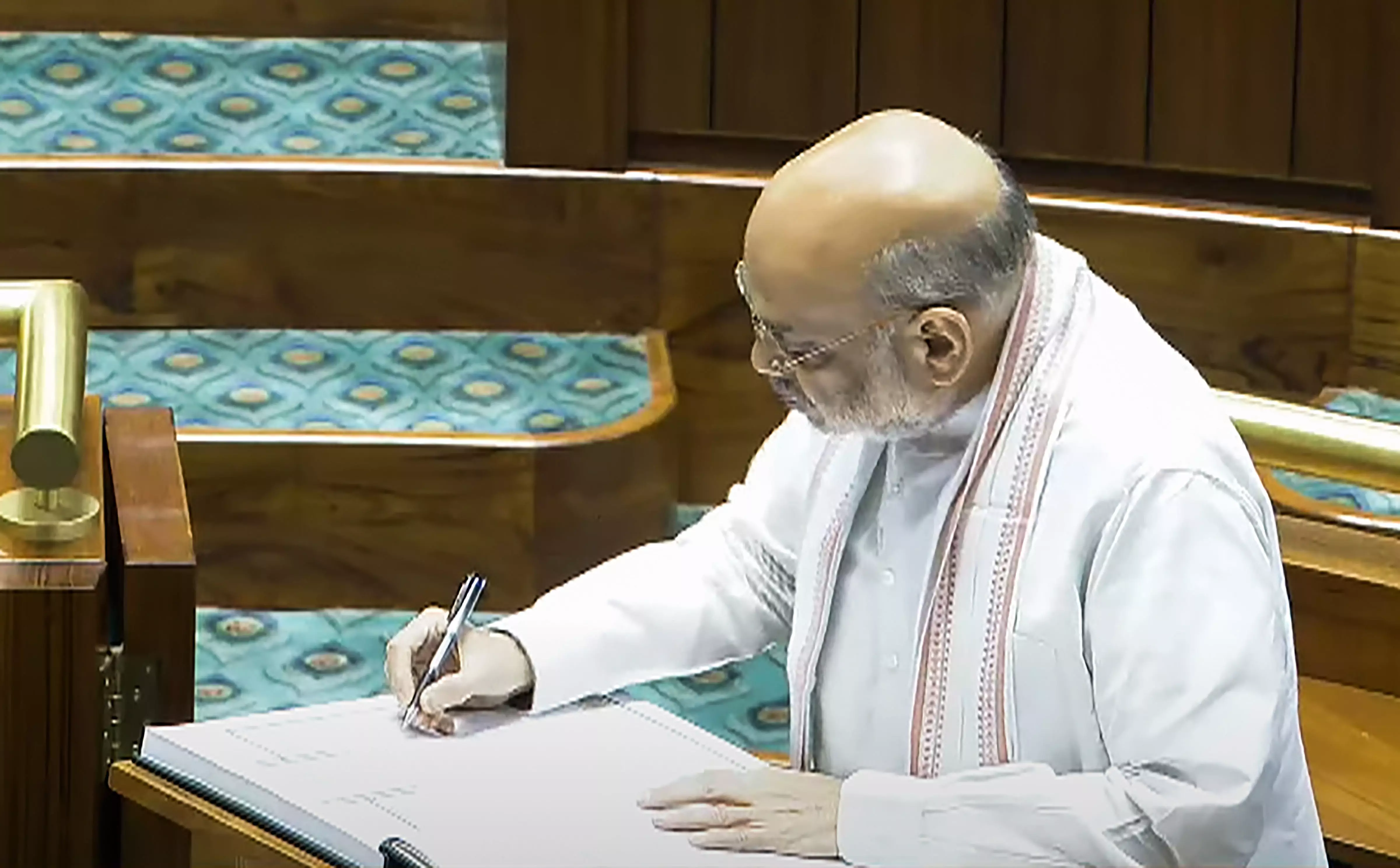 Union Home Minister Amit Shah signs a register after taking oath as a member of the House. PTI