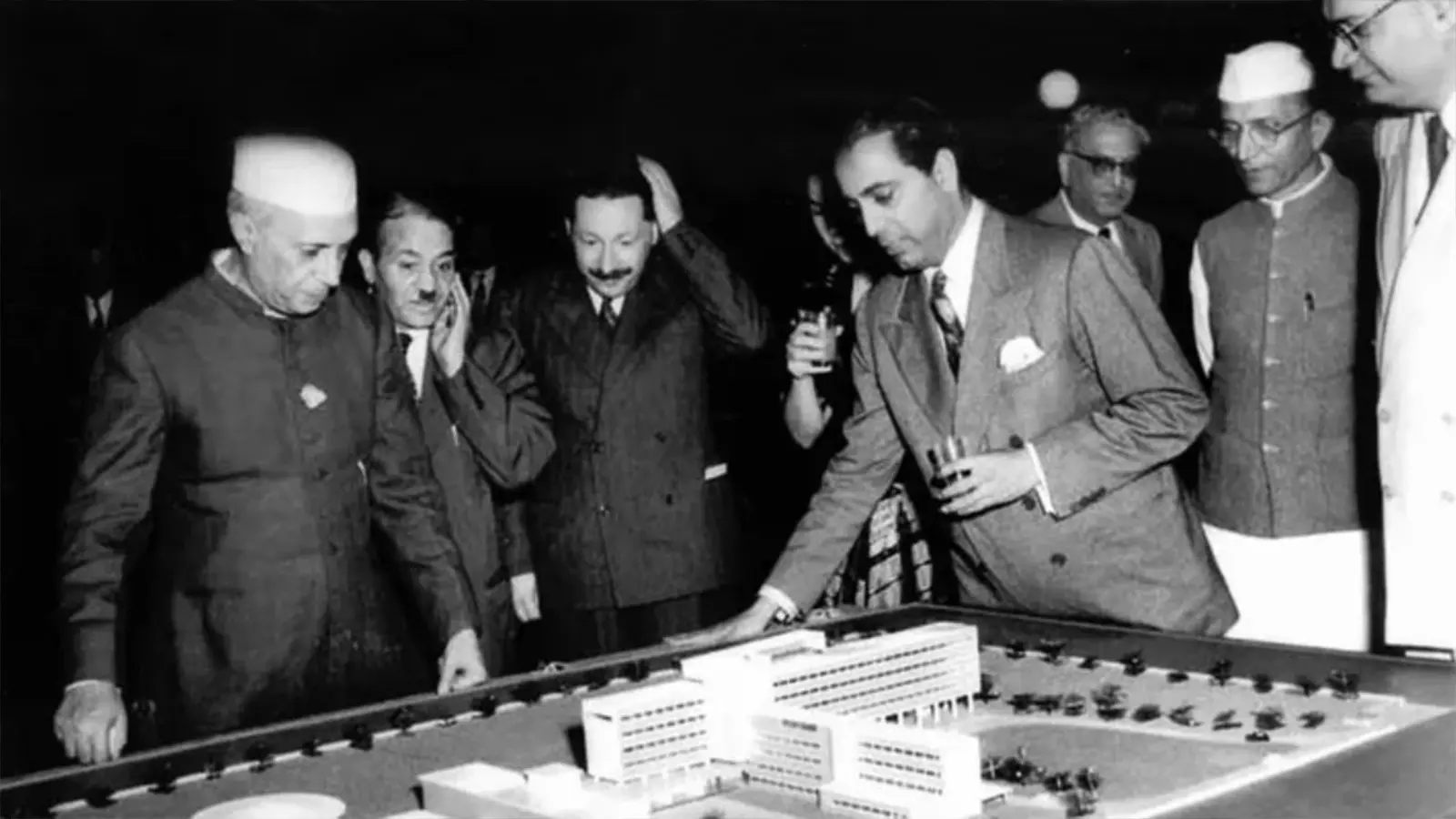 Homi Bhabha (glass in one hand and other on the table) showing Prime Minister Nehru the model of the Tata Institute of Fundamental Research.