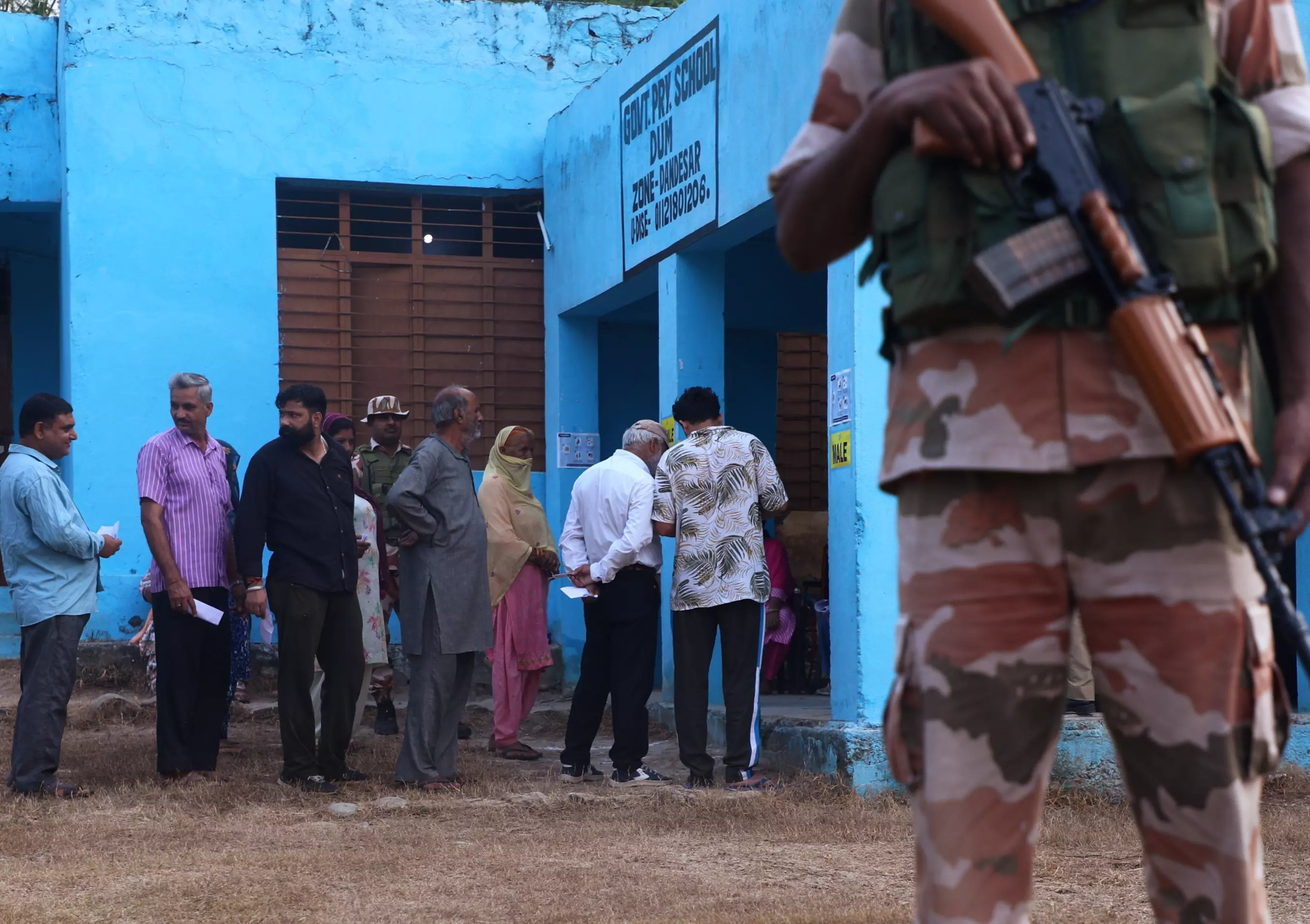 A security personnel stands guard as people wait to cast their votes at a polling station during the second phase of Jammu and Kashmir Assembly polls, at Lamberi in Nowshera, in Rajouri district, Wednesday, September 25. PTI