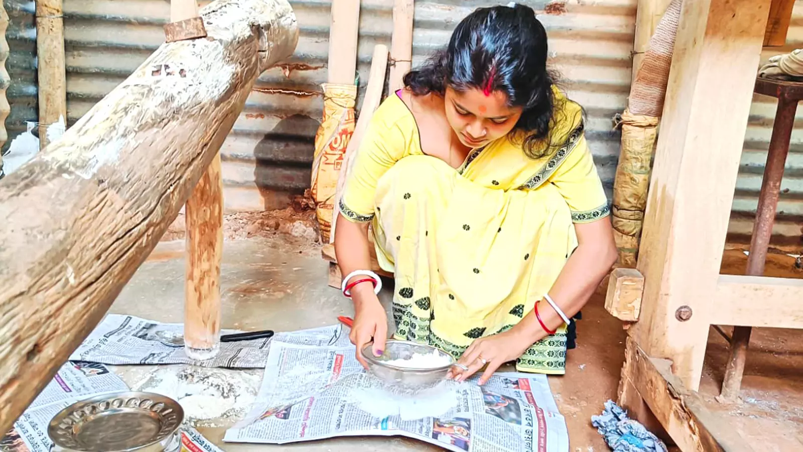 Narmada Das Chakravarty scans the flour in a sieve of any lump as the dheki pounds rice into fine powder. 