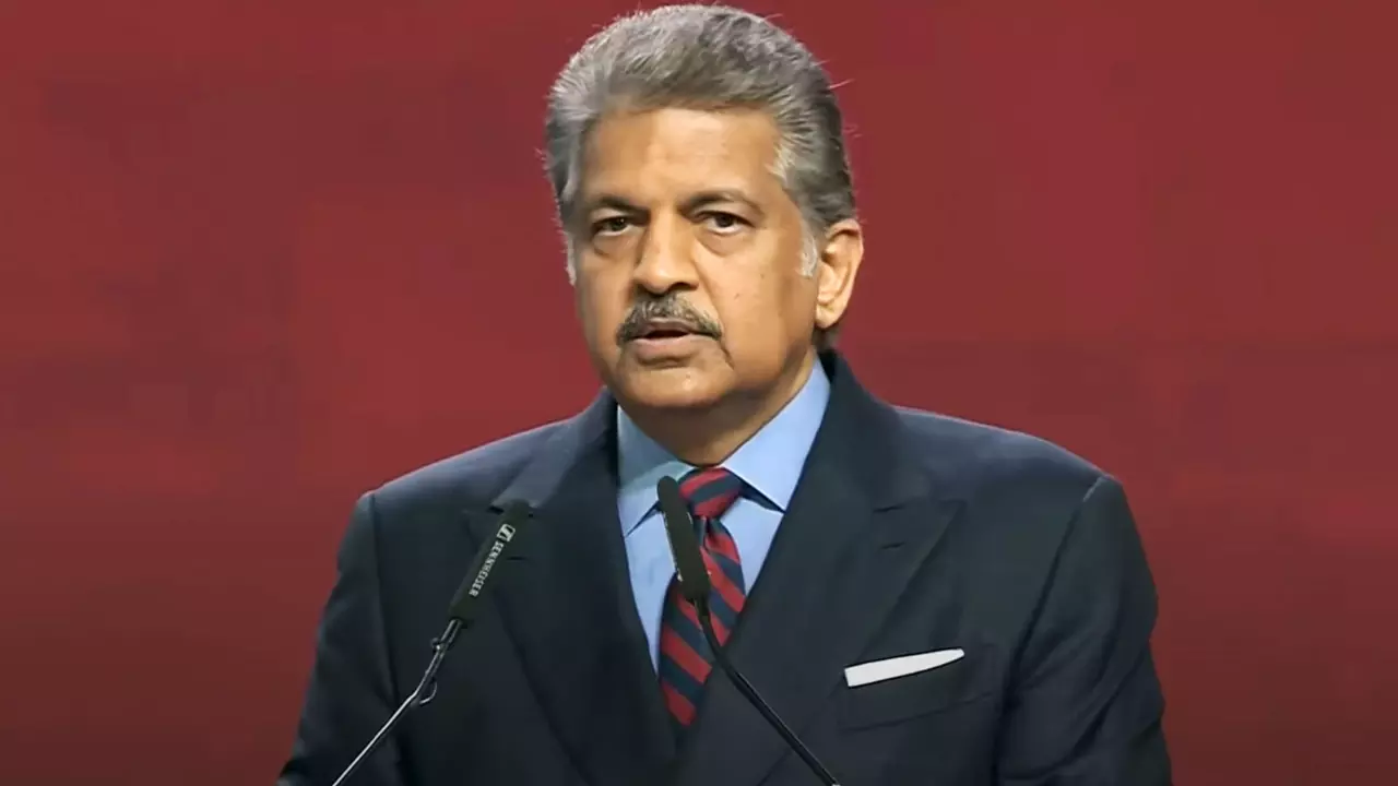 Anand Mahindra in a suit and tie speaking into a mic with a maroon background.