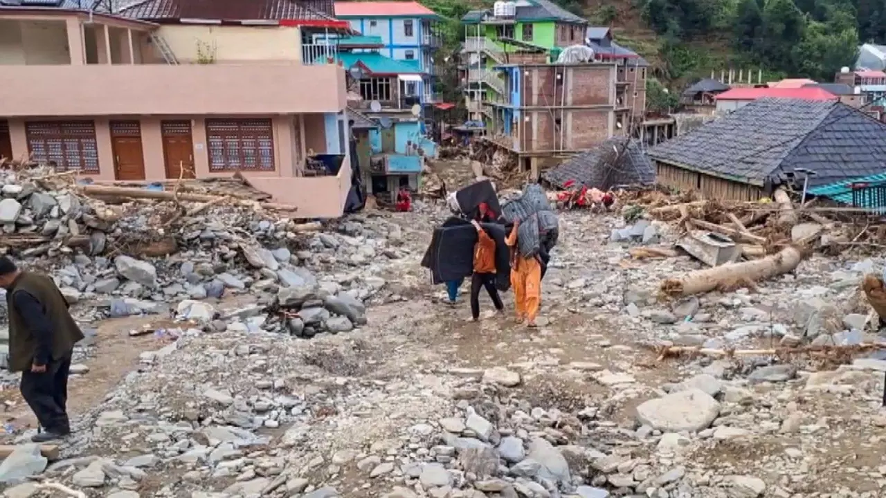 Locals carry their belongings as they walk amid the debris at a flood-affected area at Thunag in Mandi district