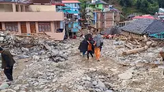 Locals carry their belongings as they walk amid the debris at a flood-affected area at Thunag in Mandi district