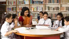 Female teachers teaching students in library at school