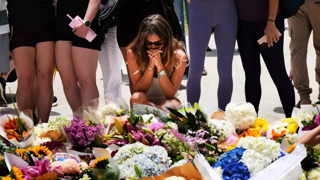 A woman kneels and prays at a flower memorial to shooting victims