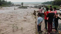 People gather near an overflowing causeway as the swollen Bin river flows following incessant heavy rainfall, in Rishikesh, Uttarakhand